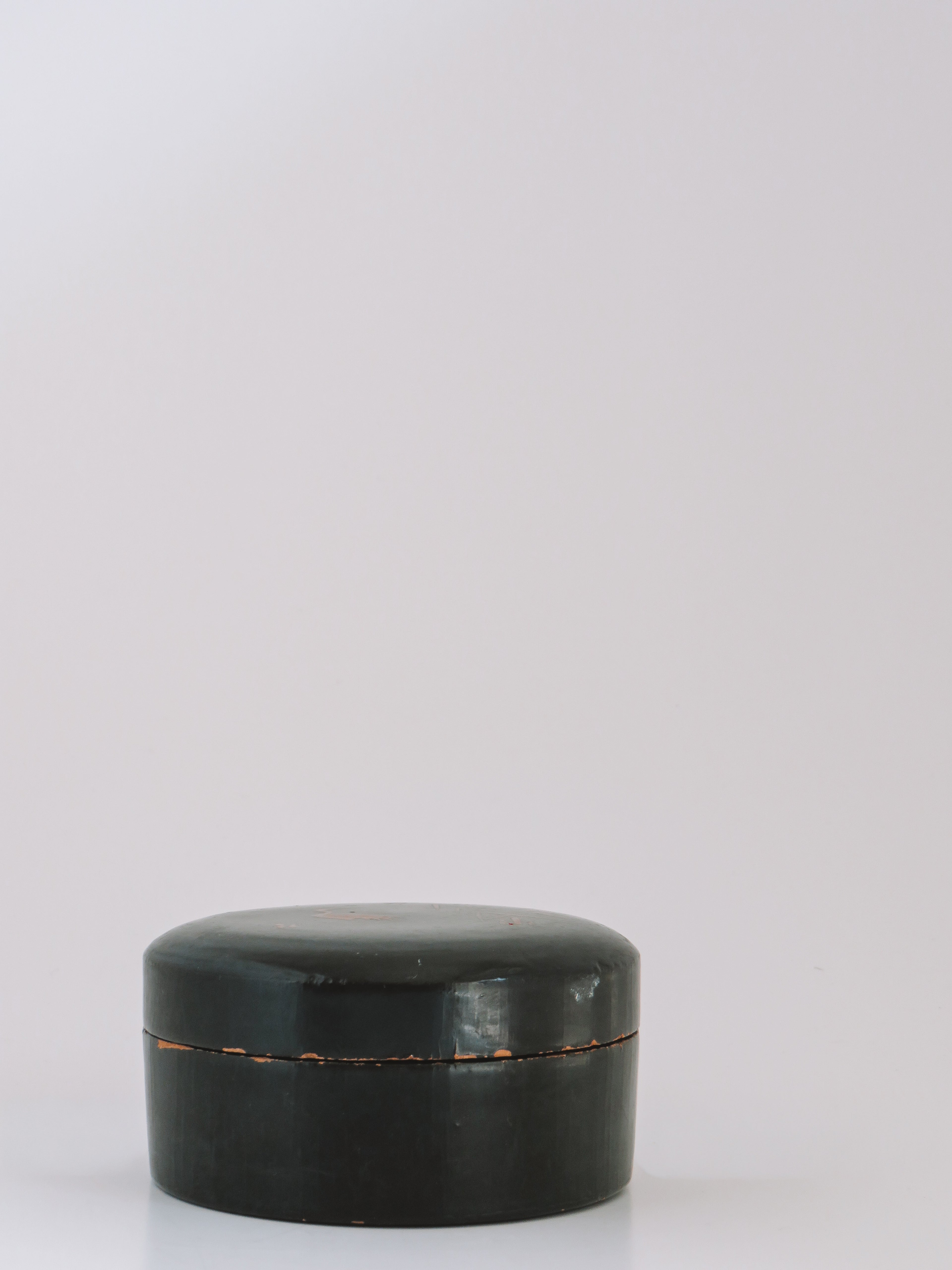 A small round black lacquered box with a lid, photographed on a clean white studio background.