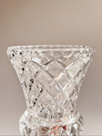 A clear cut-crystal vase with a diamond-patterned faceted design, shown against a warm beige gradient background.