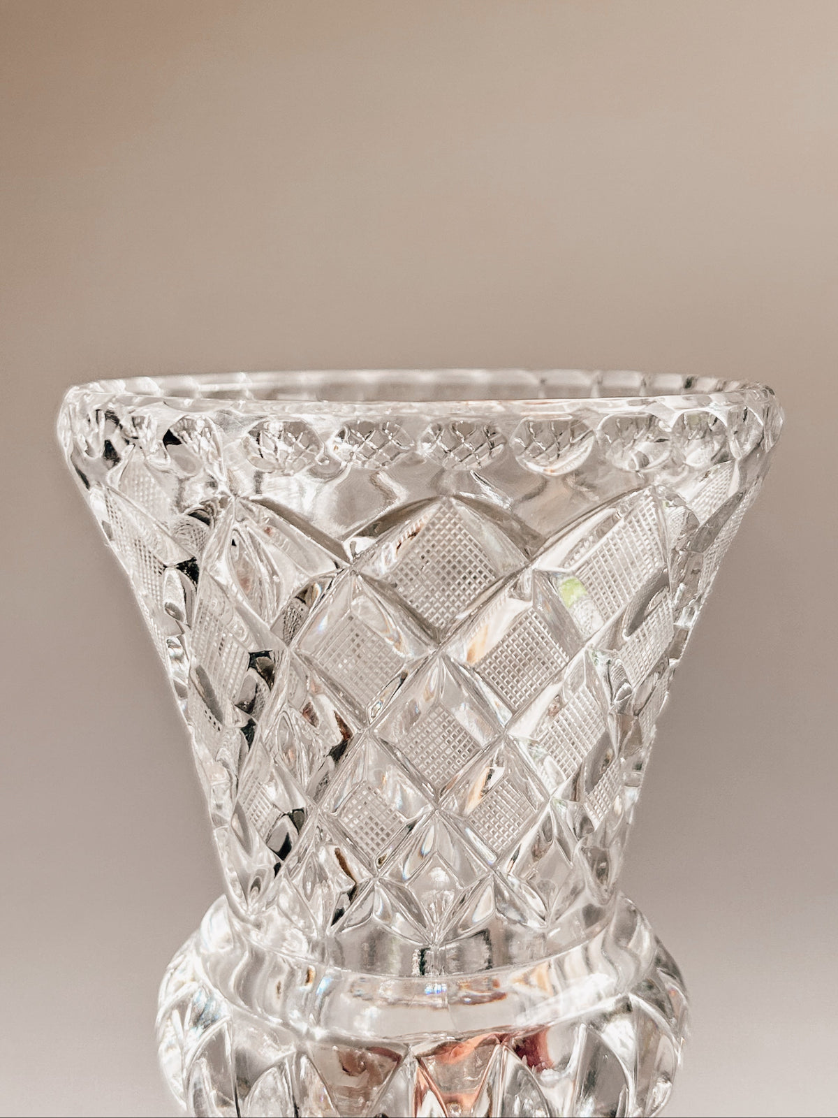 A clear cut-crystal vase with a diamond-patterned faceted design, shown against a warm beige gradient background.