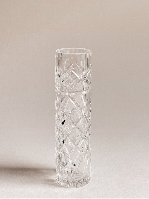 A clear cut-crystal vase with a diamond-patterned design, standing on a neutral beige surface against a matching beige background.