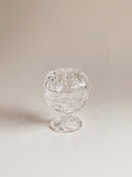 A clear cut-glass or crystal footed bowl with a lid, photographed on a warm beige studio background.