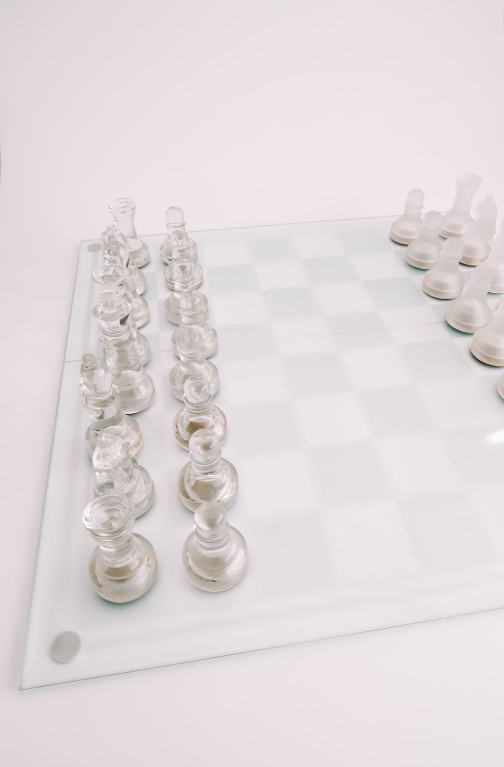A glass chessboard with transparent glass chess pieces arranged on a clean white background.