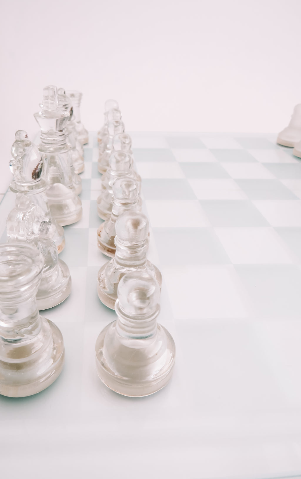 Clear glass chess pieces arranged on a white and pale blue checkered chessboard against a bright white background.