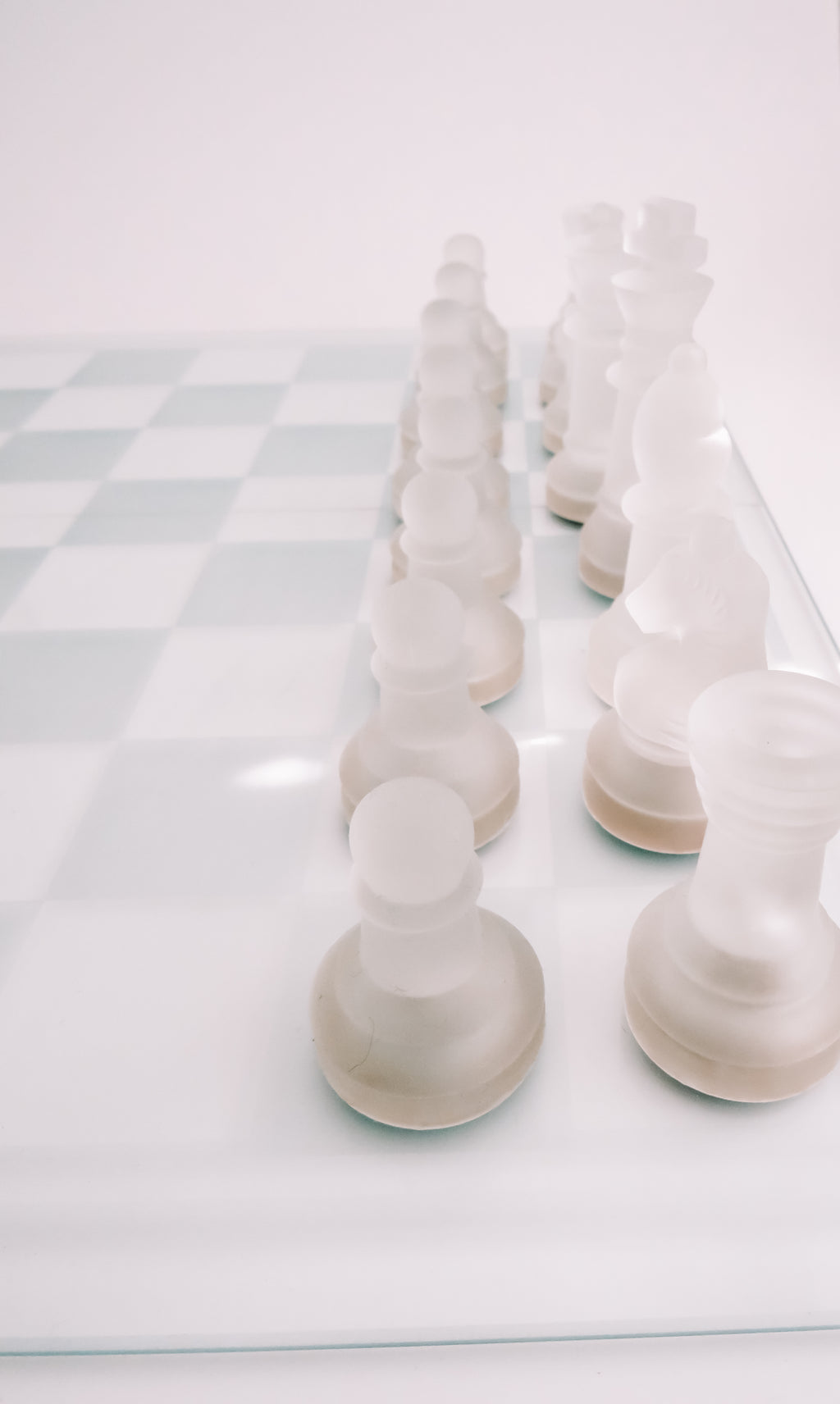 Frosted white chess pieces arranged on a glass chessboard against a clean white background.