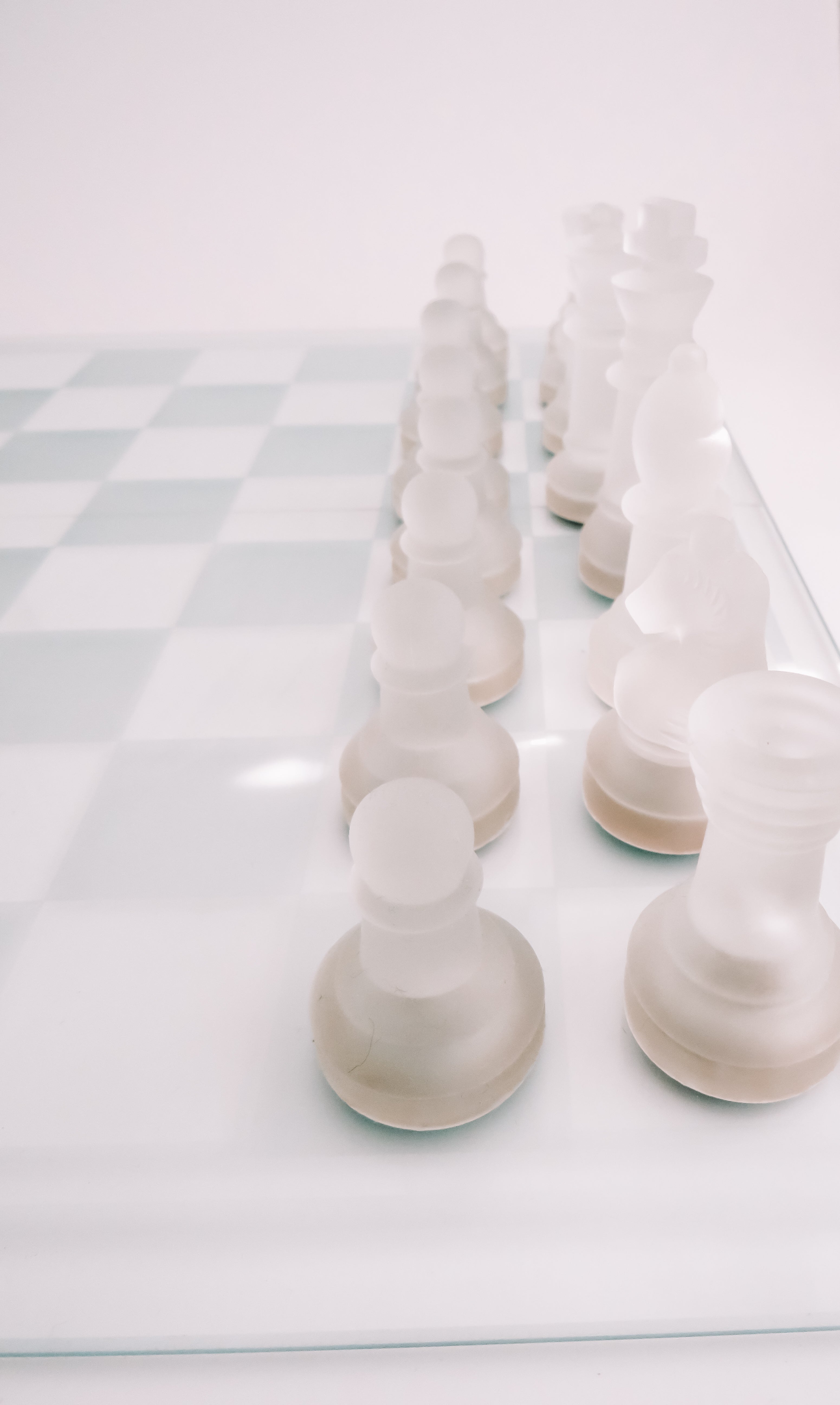 Frosted white chess pieces arranged on a glass chessboard against a clean white background.
