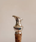 A close-up of a metallic silver corkscrew handle with a cork stopper, set against a solid warm beige background.