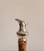 A close-up of a metallic silver corkscrew handle with a cork stopper, set against a solid warm beige background.