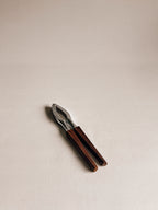 A small hand tool with dark brown wooden handles and a silver metal head, photographed on a plain light beige background.