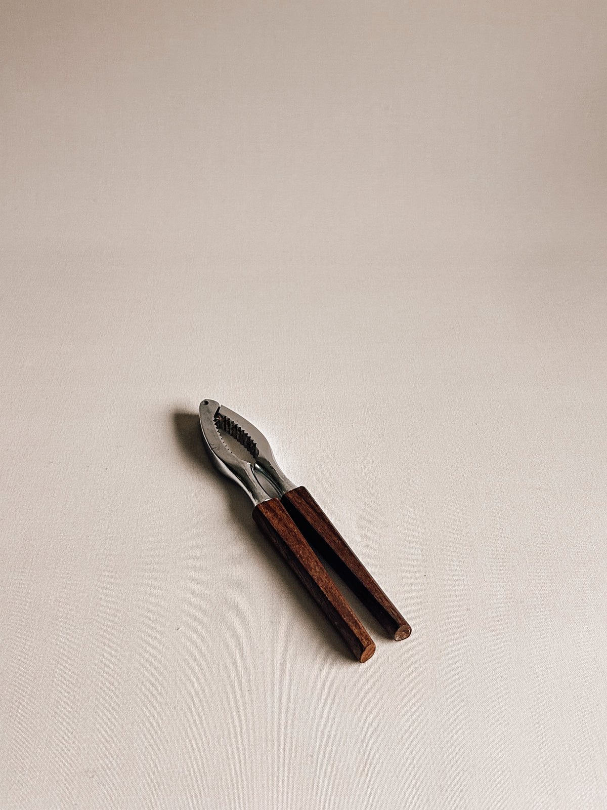 A small hand tool with dark brown wooden handles and a silver metal head, photographed on a plain light beige background.