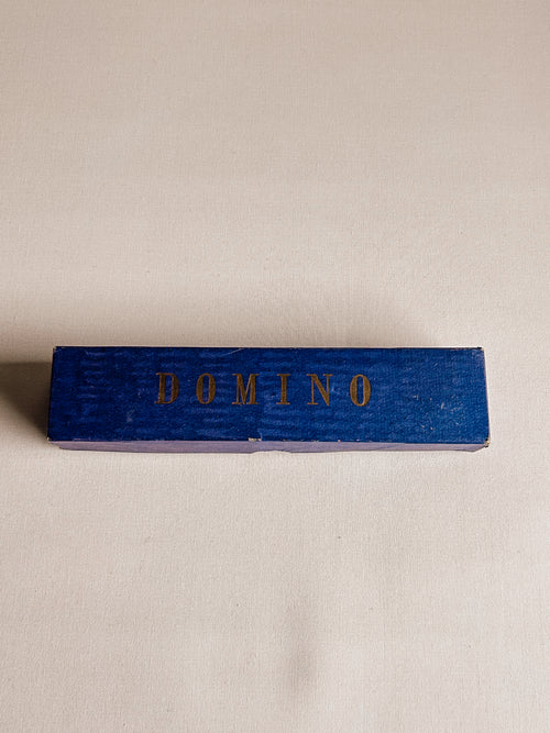 A small rectangular blue wooden box with the word 'DOMINO' printed in gold across the top, photographed on a plain light beige background.