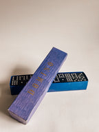 A blue domino game set with a textured blue wooden domino piece labeled 'DOMINO' in gold lettering, resting on top of two blue domino boards with white dominoes visible.