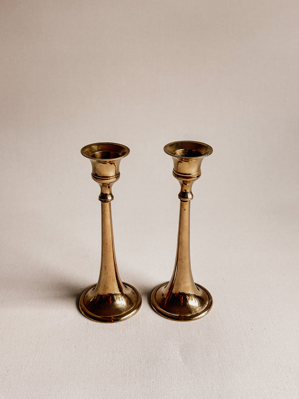 A pair of vintage brass candlesticks with a warm gold finish, standing side-by-side on a plain off-white background.