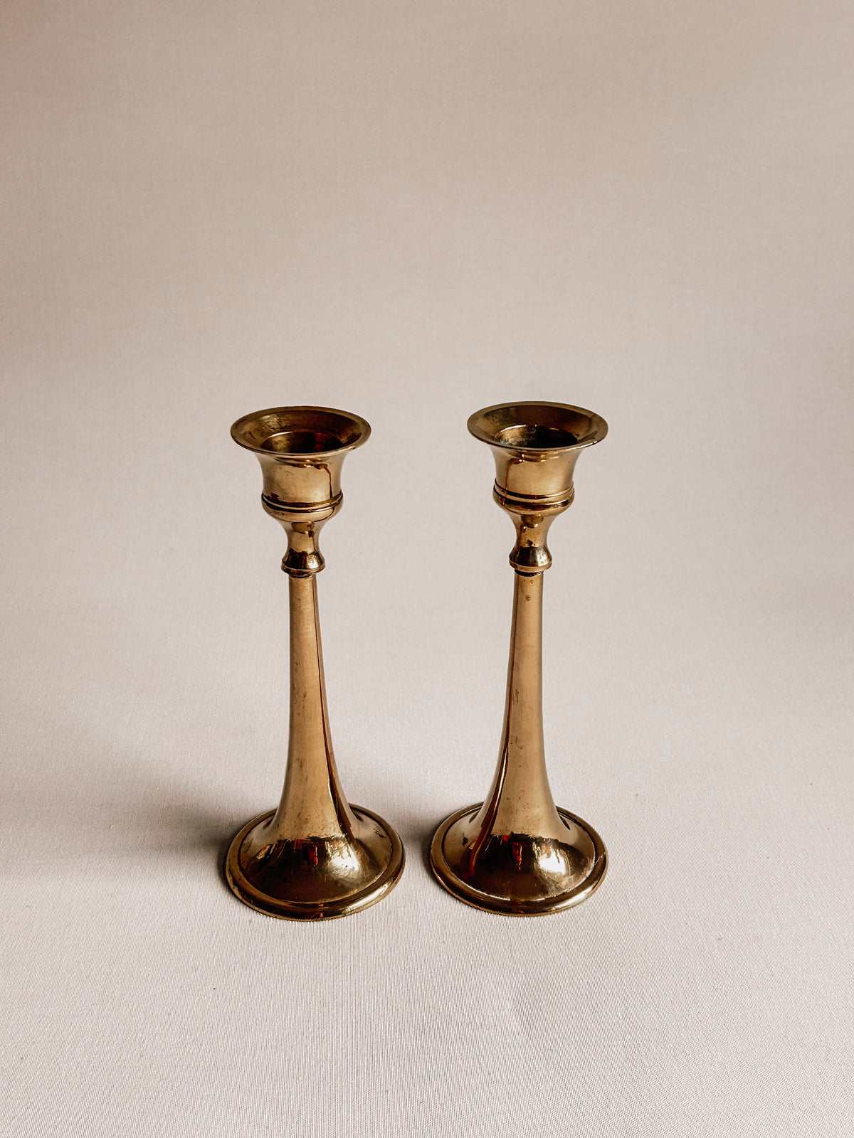 A pair of vintage brass candlesticks with a warm gold finish, standing side-by-side on a plain off-white background.